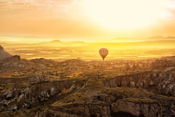 Fantastic sunrise in a valley with rocks and a hot air balloon against the backdrop of a dramatic sky. View from a height of the rock massifs. Cappadocia. Turkey. - Foto, afbeelding