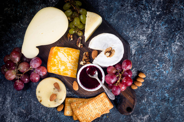 Assorted homemade pieces cheese with jam, grapes, cookies and nuts, cookies and nuts on table.  Fresh dairy product, cheese snack, healthy organic food. Delicious appetizer. - Photo, image