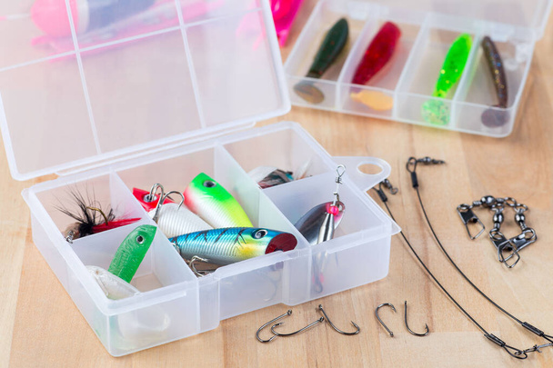 Various fishing lures in plastic box and fishing accessories on a wooden background, horizontal - Foto, Imagen