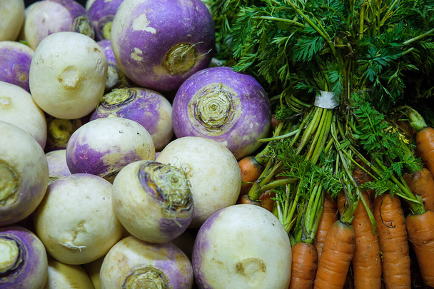 Pile of fresh brassica rapa or turnips and bundles of small carrots with leaves at the Farmer's market or grocery store, delicious root vegetables packed with nutrients, consumed both raw and cooked - Photo, Image