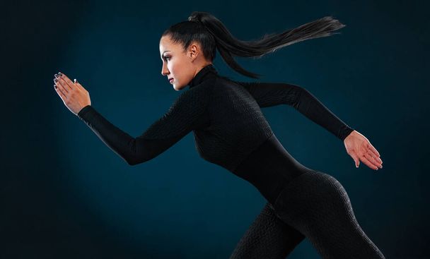 Strong athletic woman sprinter, running on black background wearing in the sportswear and headphones. Fitness and sport motivation. Runner concept. - Foto, afbeelding