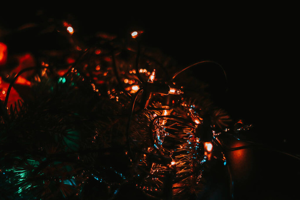 Σκούρα φωτογραφία με μια πλήρη σειρά από χρωματιστά φώτα σε μαύρο φόντο δημιουργεί ένα υπέροχο πνεύμα των προσεχών Χριστουγέννων. Κόκκινο, πορτοκαλί, μπλε, πράσινο και πολλά άλλα. Μια ειρηνική χριστιανική διακοπές - Φωτογραφία, εικόνα