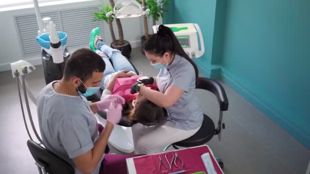Tıbbi maskeli iki dişçi, dişçi muayenehanesinde bir erkek ve bir kadın dişlerini ameliyat ediyorlar. Diş hekimliği. Sağlık ve Tıp Konsepti 'nden. Ağır çekim. Üst görünüm. - Video, Çekim