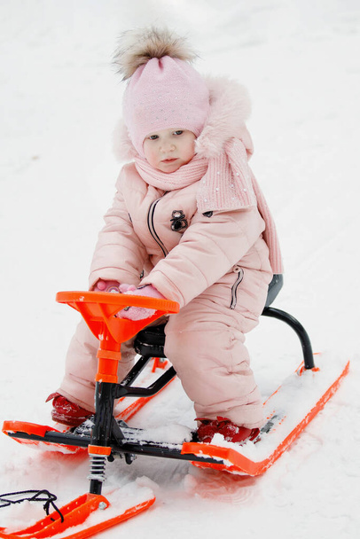 Chica de color rosa en un trineo naranja en invierno en la nieve blanca. - Foto, Imagen
