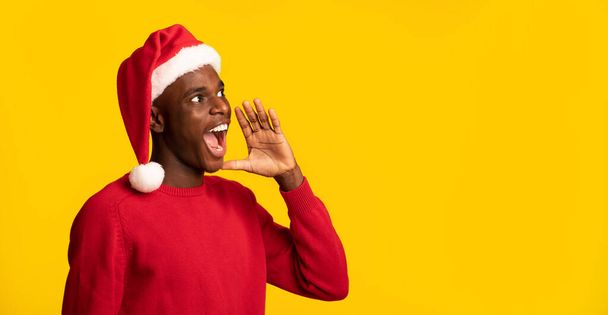Zwarte man in Santa Hoed schreeuwen op kopieerruimte, het maken van kerstaankondiging - Foto, afbeelding