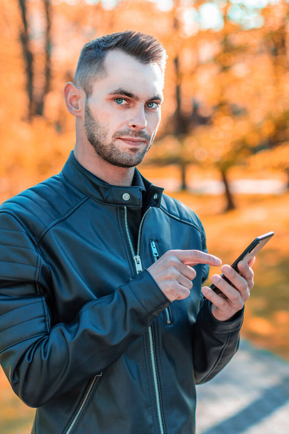 秋の公園でスマートフォンを使うハンサムな男 - 写真・画像