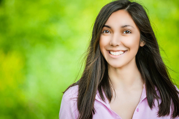 Een portret van een mooie Aziatische vrouw die glimlacht naar de camera. Tegen de achtergrond van een groen zomerpark. - Foto, afbeelding