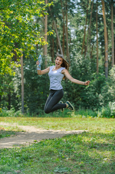 Νεαρή όμορφη γυναίκα πηδάει πάνω στο φόντο ενός πράσινου πευκοδάσους. - Φωτογραφία, εικόνα