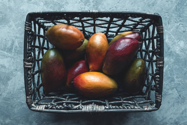 large mangoes in a wicker basket on a gray background. Healthy food, vegan - Foto, imagen