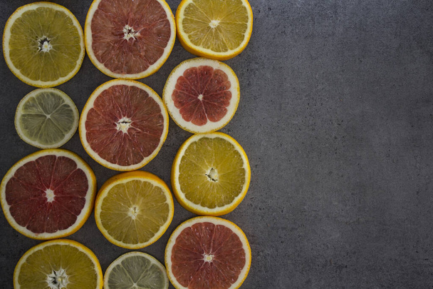 Fruit frame or border. Fresh juicy orange, lemon and grapefruit slices on a table. Dark gray background with copy space. Healthy eating concept.   - Photo, Image
