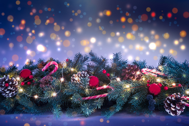 Ozdobiona i oświetlona girlanda świąteczna z gałązkami jodły na tle rozmytych świateł w nocy. - Zdjęcie, obraz