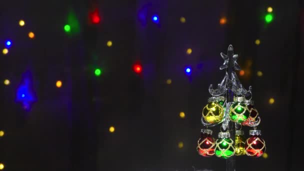 Glazen kerstboom met kerstspeelgoed op de achtergrond van knipperende lichten - Video