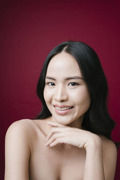 Portret pięknej azjatyckiej modelki z czarnymi włosami i zdrową skórą na czerwonym tle. - Zdjęcie, obraz