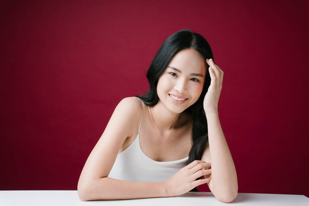 Hübsche junge asiatische Frau mit natürlichem Make-up schaut in die Kamera direkt isoliert auf rotem Hintergrund. - Foto, Bild