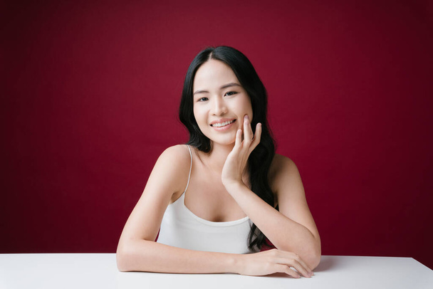 Portret van schoonheid aziatische vrouw met perfecte natuurlijke huidverzorging glimlachen op camera geïsoleerd op rode achtergrond. - Foto, afbeelding