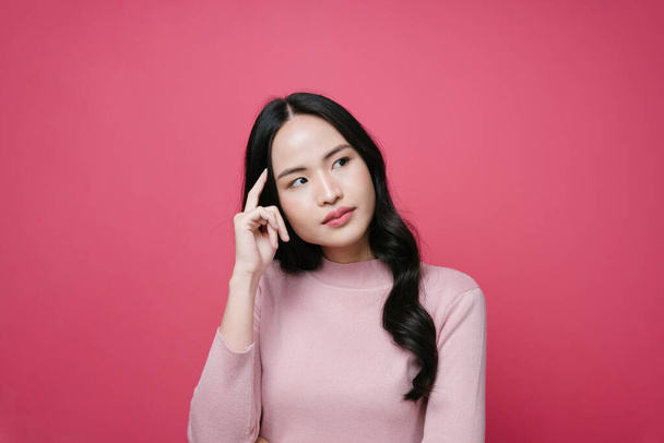 Porträt einer jungen asiatischen Frau mit nachdenklichem Ausdruck isoliert auf rosa Hintergrund. - Foto, Bild
