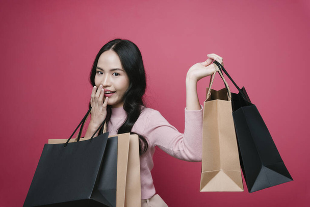 Asiatique amateur de shopping aiment acheter des choses dans le centre commercial. Shopaholic fille tenant de nombreux sacs en papier isoler sur fond rose. - Photo, image