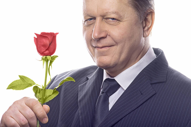 Romantic senior gentleman holding a rose and looking at camera. Isolated on white background. - Zdjęcie, obraz