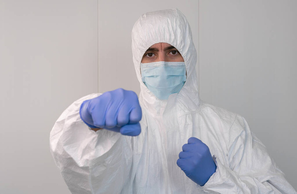 A male nurse in a protective suit PPE on guard striking a punch to fight the Coronavirus. Concept of fight against the pandemic caused by Covid-19. - Fotografie, Obrázek