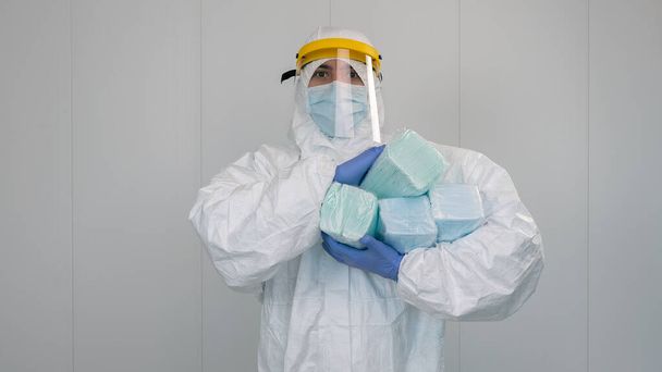 Un'infermiera in tuta protettiva PPE porta tra le braccia diverse confezioni di nuove maschere. Il medico indossa una maschera per prevenire il coronavirus. - Foto, immagini