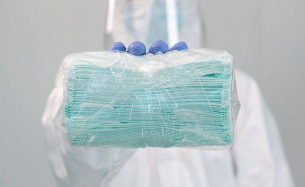 Mannelijke verpleegster draagt beschermend pak met plastic gezichtsscherm toont een pakket van nieuwe medische maskers tijdens een pandemie van covid-19 in een ziekenhuis in Spanje. Interieur van medisch centrum. Coronavirusepidemie. - Foto, afbeelding