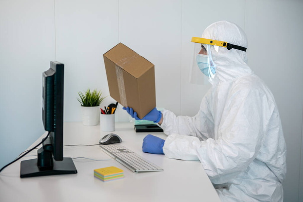 Медсестра носит СИЗ и пластиковый щит для лица, используя компьютер, чтобы отправить заказ на новые медицинские маски во время пандемии ковида 19 в больнице Испании. Интерьер клиники установки коронавирусной эпидемии - Фото, изображение