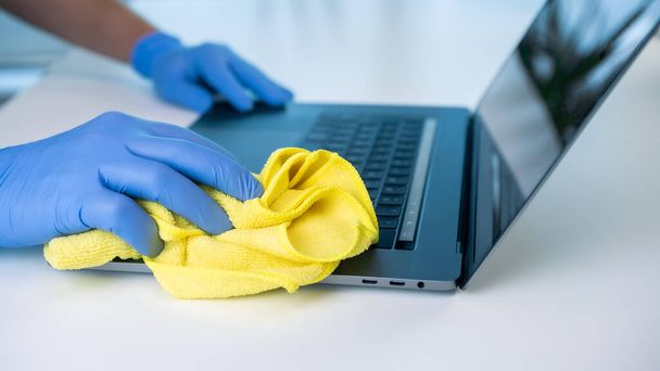 Een persoon met handschoenen reinigt de laptop om het coronavirus te voorkomen. Desinfectie en reiniging van een werkruimte. - Foto, afbeelding