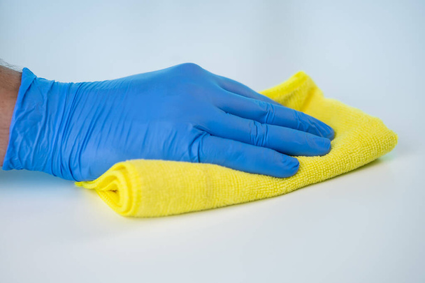 A healthcare worker is cleaning and disinfecting his workspace to prevent the spread of the coronavirus. Using gloves and a cloth to wipe the table. - Zdjęcie, obraz