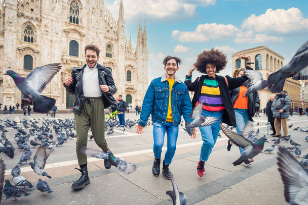 ミラノのドゥオモ広場を走る4人の友人のグループは、一緒に楽しい気分でお祝いし、笑っています - 写真・画像