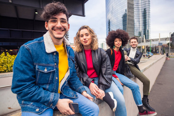 Gruppe von vier befreundeten Touristen multiethnisch sitzen draußen aussehende Kamera lächelnd die Zeit zusammen genießen Spaß im Urlaub Sightseeing in der Stadt - Foto, Bild