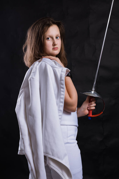 Teenage girl fencer dressed in uniform with epee and helmet - Фото, изображение