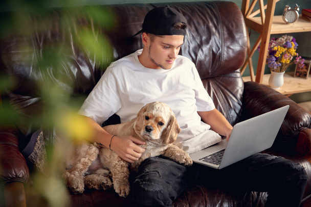 Young man working on laptop computer sitting at home with a dog pet and leaning during Coronavirus or Covid-19 quarantine - Foto, Imagem