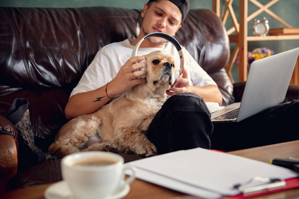 Молодий чоловік сидить вдома зі своїм собачим улюбленцем і слухає музику під час Коронавірусу або Ковід-19 карантину. Концепція життя. - Фото, зображення