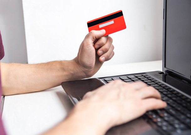 Homem de compras on-line para dia dos namorados com cartão de crédito no laptop. Close up de um homem mãos segurar um cartão de crédito vermelho perto de um laptop - Foto, Imagem