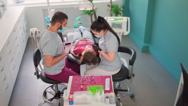 Zwei Zahnärzte in medizinischen Masken, ein Mann und eine Frau in einer Zahnarztpraxis, führen eine Operation an den Zähnen durch. Zahnmedizin. Gesundheits- und Medizinkonzept. Zeitlupe. Ansicht von oben. - Filmmaterial, Video