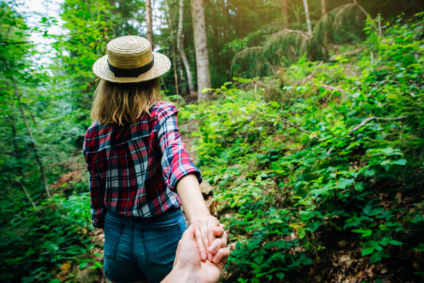 山の中で写真を撮ってください。チェック柄のシャツと藁帽子のスタイリッシュな女性。欲望の概念。カップルハイキングや夏に旅行。自然の中で手を握る. - 写真・画像