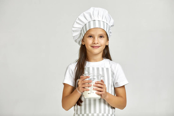 little girl in chef hat and apron with flour in measuring cup. - Foto, Bild
