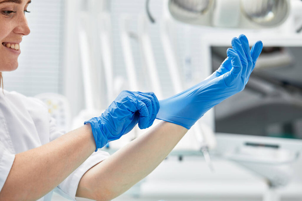 Una dentista femenina se pone guantes contra un fondo de equipo dental en un consultorio dental. Concepto de paciente y dentista feliz. - Foto, imagen