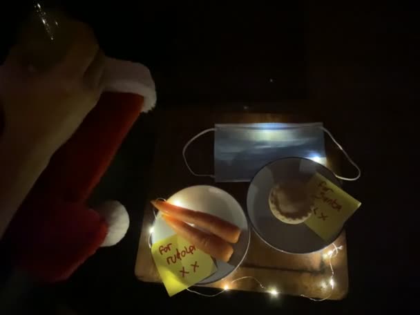 covid-19 Nochebuena, sombrero de santa con mascarilla y para nota de Santa con pastel de carne picada y zanahorias para Rudolph en nota de escritura infantil   - Imágenes, Vídeo