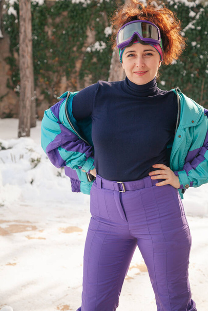 beautiful young woman in ski goggles and overalls stands against the backdrop of tall trees. The snow is white. A female portrait without retouching with her natural imperfection - Foto, imagen