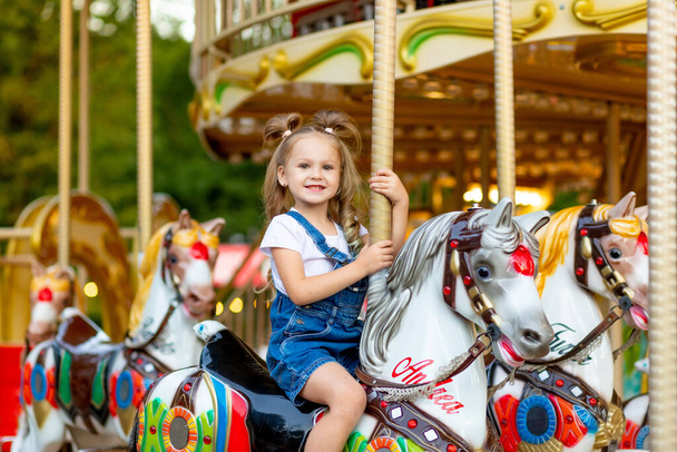 幸せな赤ちゃんの女の子は夏に遊園地で馬にカルーセルに乗って - 写真・画像