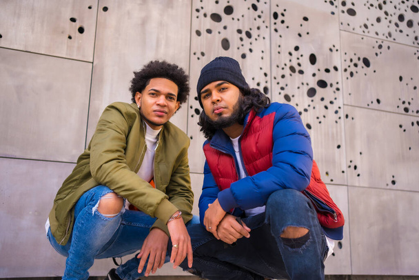 Urban style, portrait of two Latino black friends having fun in the street. Afro hair boy, brunette boy with long hair with hat - Fotografie, Obrázek