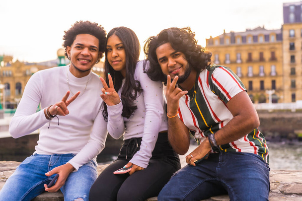 Lifestyle, portrait of three black friends having fun in the city with the sunset in the background, slimming and millennial in the city. Afro hair boy, brunette boy with long hair and brunette girl - Photo, image