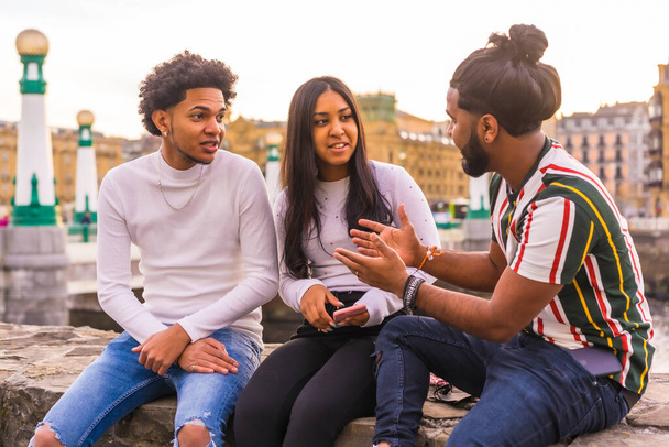 Lifestyle, three black friends having fun in the city with the sunset in the background, slimming and millennial in the city. Afro hair boy, brunette boy with long hair and brunette girl - Photo, Image