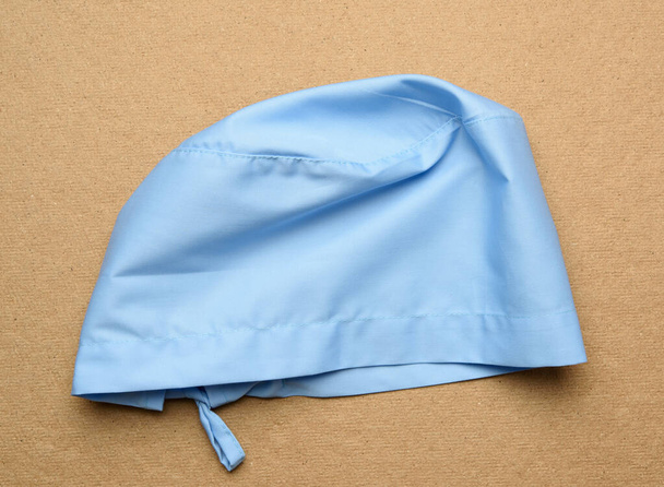 gorra médica textil azul con corbatas para médico, cirujano sobre fondo marrón, vista superior - Foto, Imagen