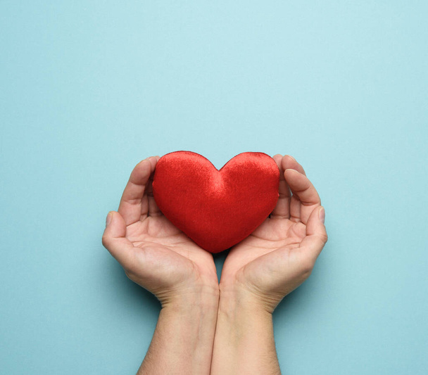 ženské ruce drží červené textilní srdce, modré pozadí. koncept lásky a darů, close up - Fotografie, Obrázek