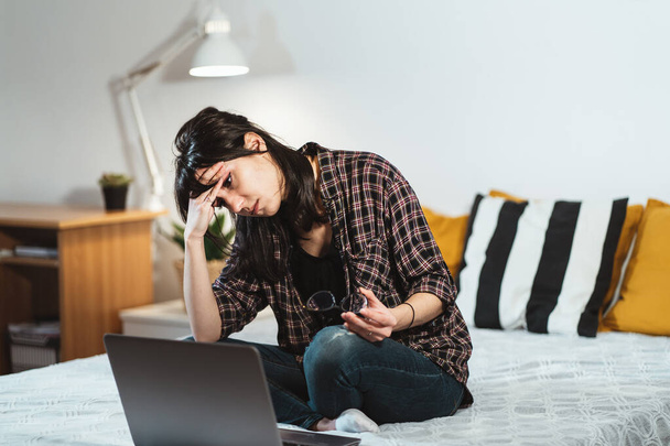 Ekose gömlekli, yorgun bir kadın gece geç saatlere kadar bilgisayar dizüstünü izlerken yüzünü ovalıyor. Başarı iş kariyeri ve mesai konsepti - Fotoğraf, Görsel