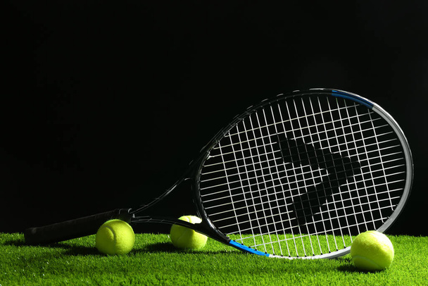 Tennis racket and balls on green grass against dark background. Sports equipment - Zdjęcie, obraz