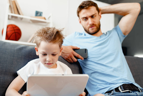 Worried father peeking at what his son is watching on digital tablet - Photo, image