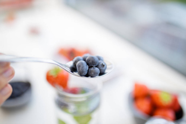 Female hand holding a spoon with blueberries above more fruit - Photo, Image